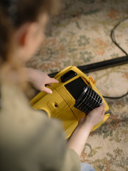 A professional cleaner from Sudbury Carpet Cleaners, dressed in a white protective suit, mask, and gloves, is performing surface cleaning with a vacuum or steam cleaning equipment on a light-colored c