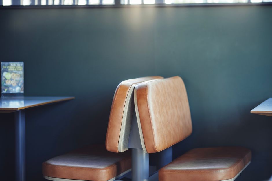 A vintage-style upholstered armchair with a pastel green frame, featuring ornate carvings, and pink fabric with printed text and logos, situated next to a small round wooden table in a cozy cafe or re